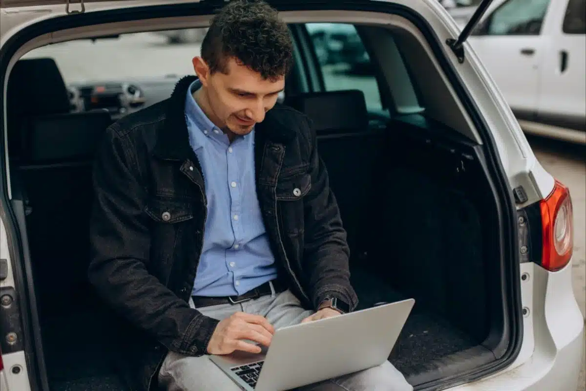 Man using laptop at car trunk