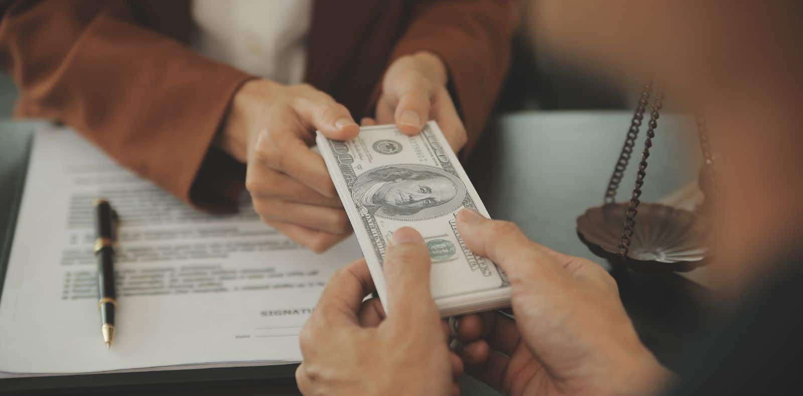 A woman with pink nails holds a single curved US $10 bill up close to the camera with a blurred background