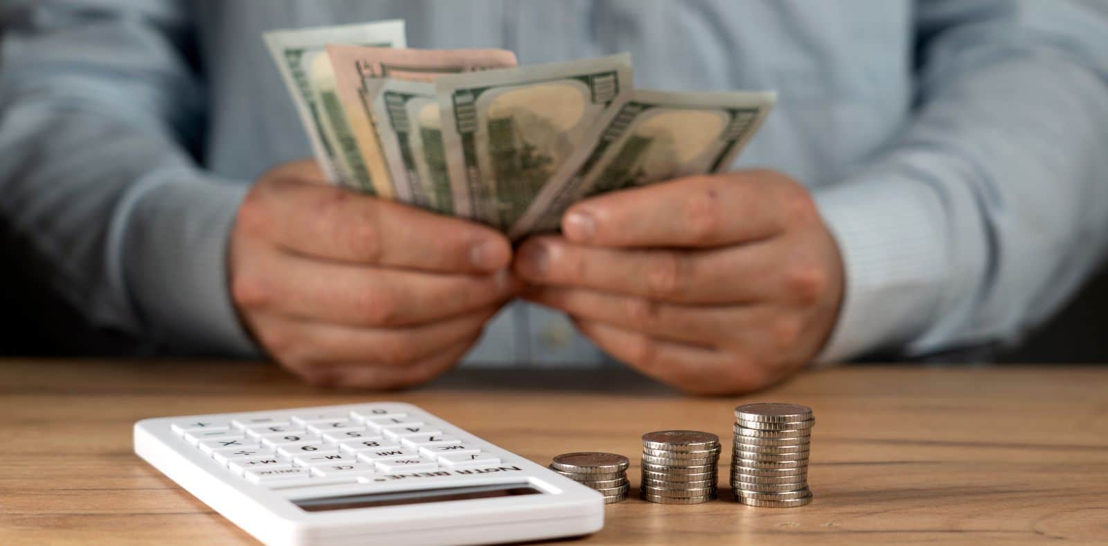 Two suited men pass €500 euro banknotes to each other across a desk with a laptop in a formal office setting
