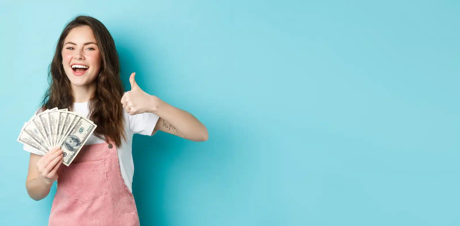 A fanned arrangement of $100 bills with three gold coins and a black calculator against a vivid blue background with copy space