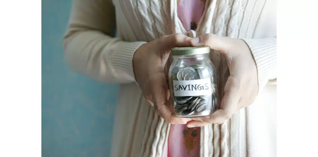 Person holding a jar filled with coins labeled savings representing personal finance and money saving.