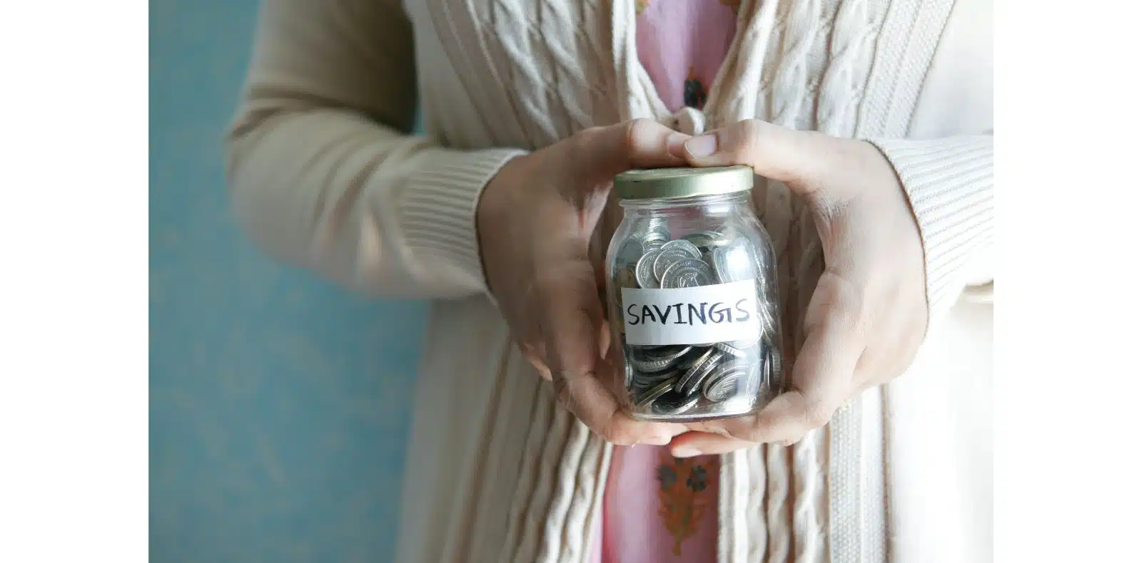 Person holding a jar filled with coins labeled savings representing personal finance and money saving.