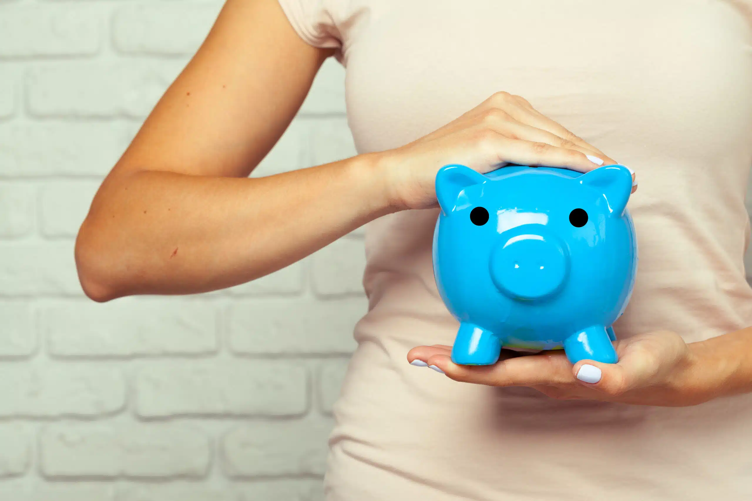 Person holding a blue piggy bank in front of a light-colored wall.