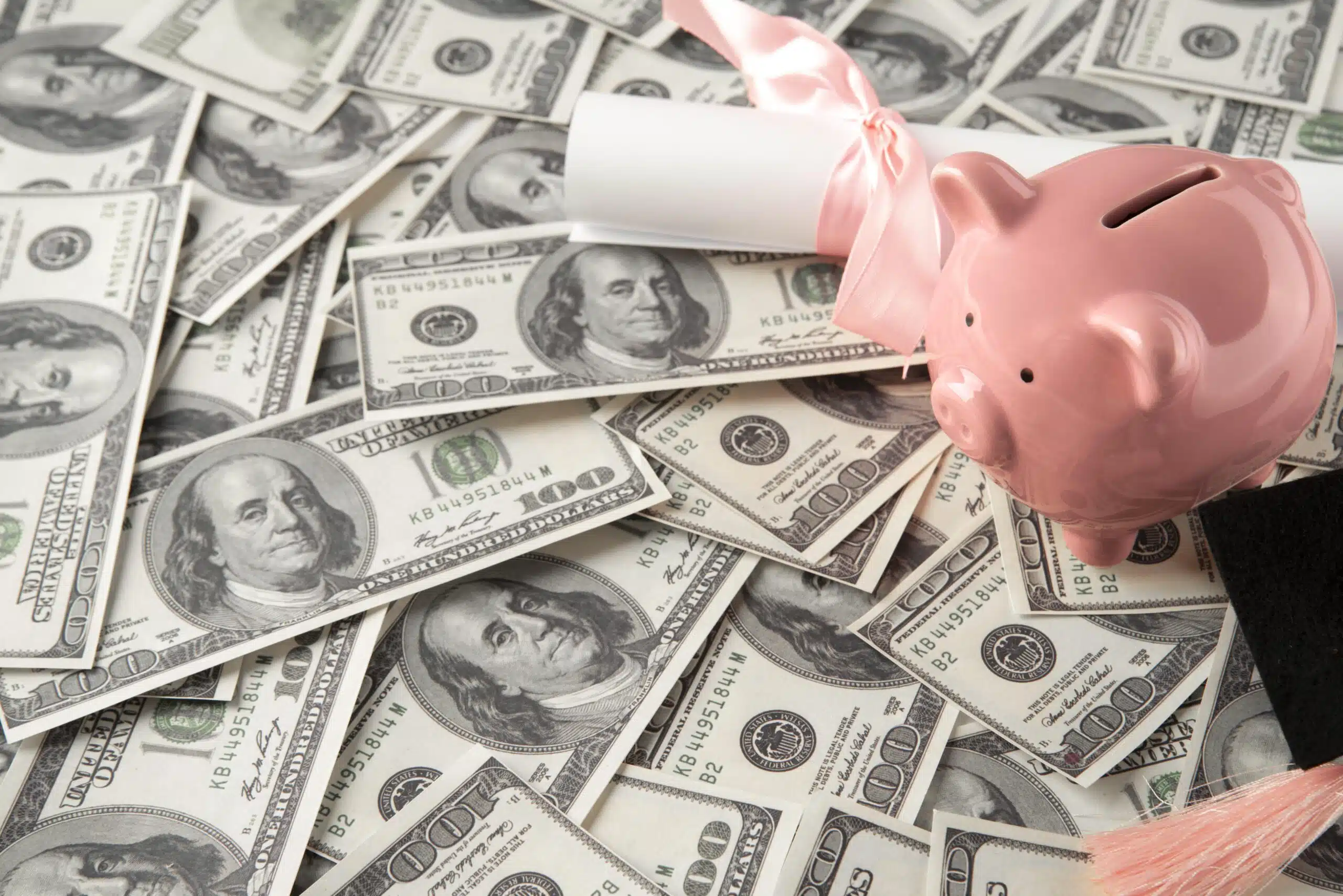 Pink piggy bank placed on top of 100-dollar bills with a decorative ribbon.